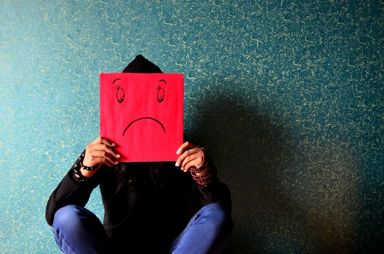 Person holding a sad face drawn on red paper in front of their face