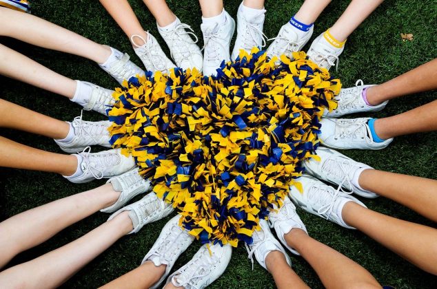 Cheerleaders sitting in a circle with pom poms in the middle