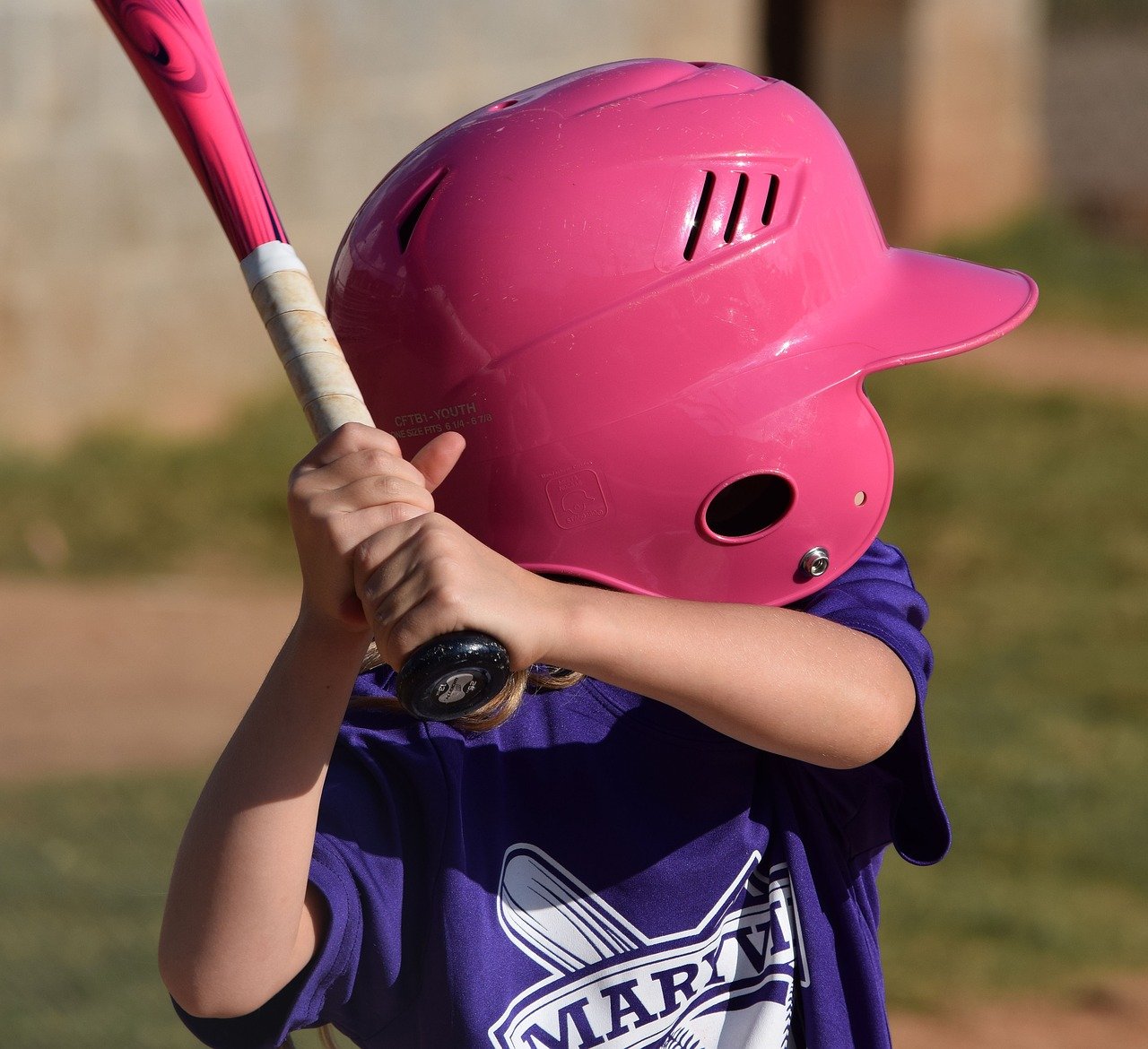 Young athlete wearing a purple team shirt and pink helmet