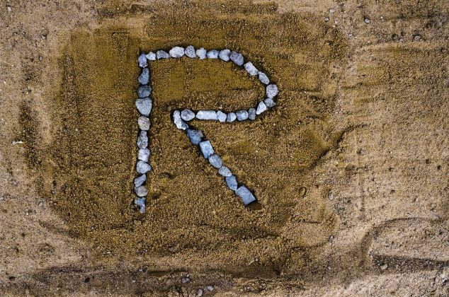 Letter "R" drawn in rocks on sand