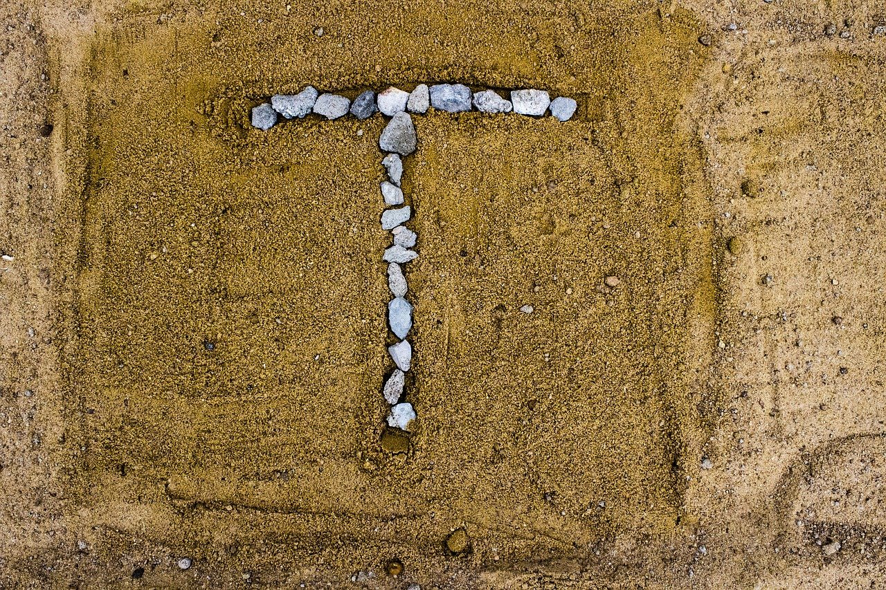 Letter "T" drawn in rocks on sand