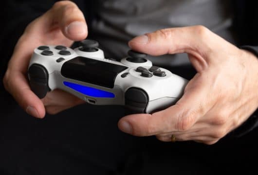 Man's hands holding a PlayStation controller playing Persona 5