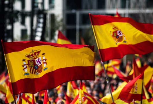Multiple Spanish flags waving above a crowd of people