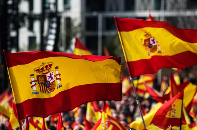 Multiple Spanish flags waving above a crowd of people